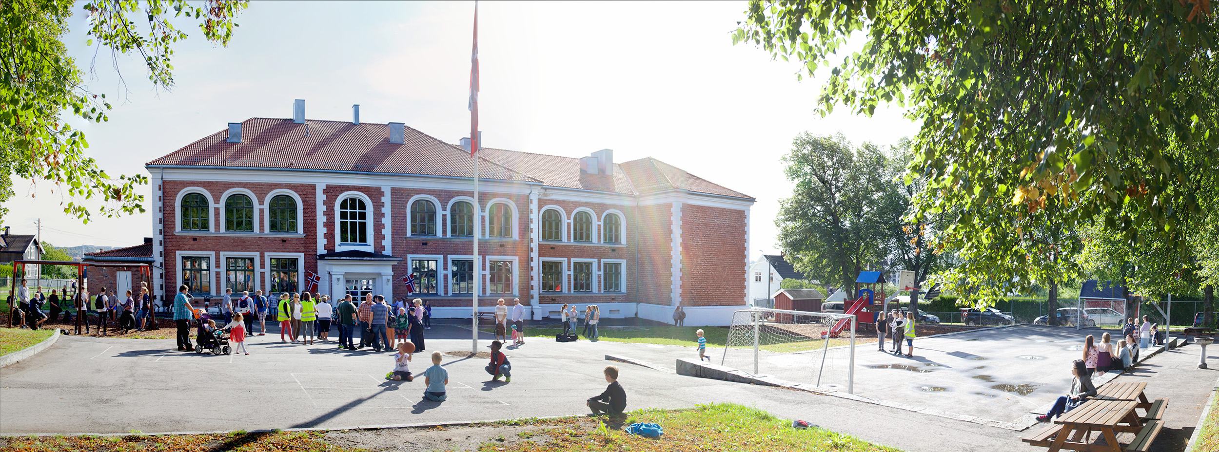 Skolestart utenfor Torderød skole med norsk flagg, foreldre og barn